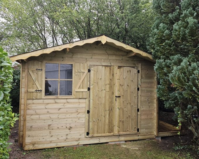 Abri de jardin en bois neuf avec volets et arbres.