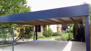 Carport moderne bleu foncé avec structure bois, devant une maison.