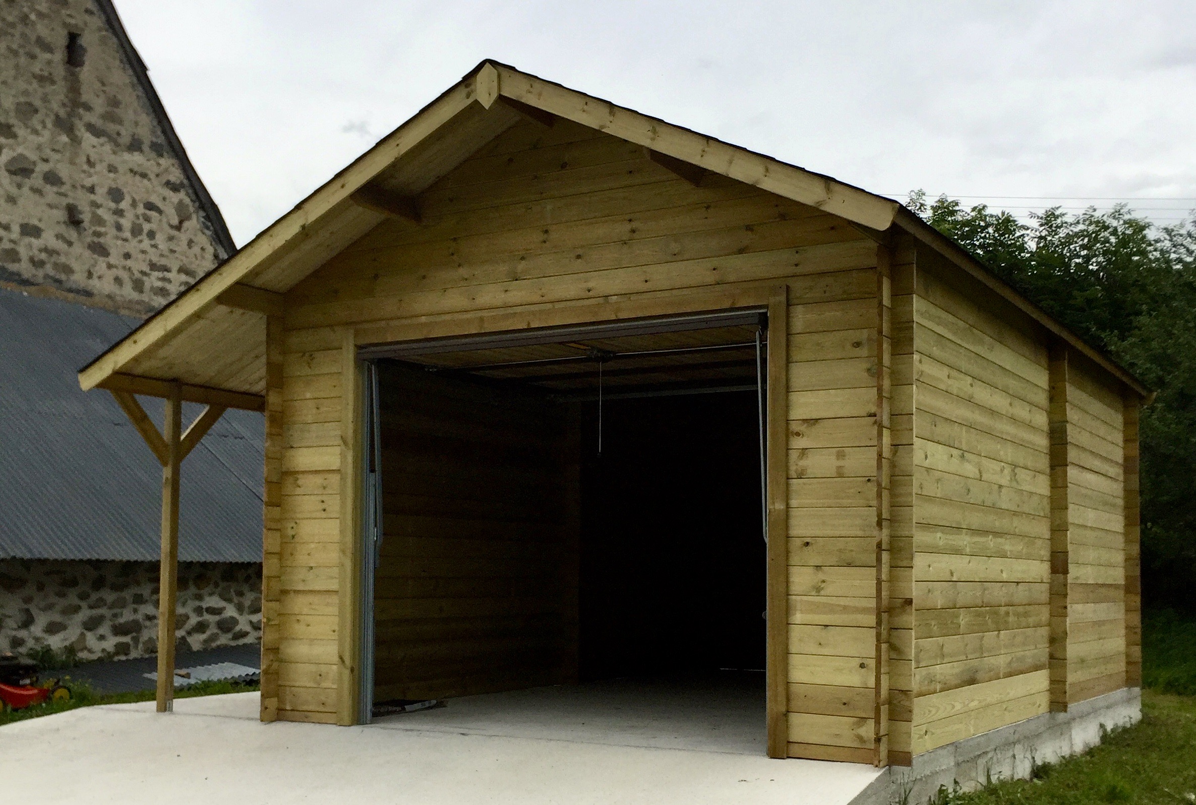 Nouveau garage en bois avec porte ouverte et toiture inclinée.
