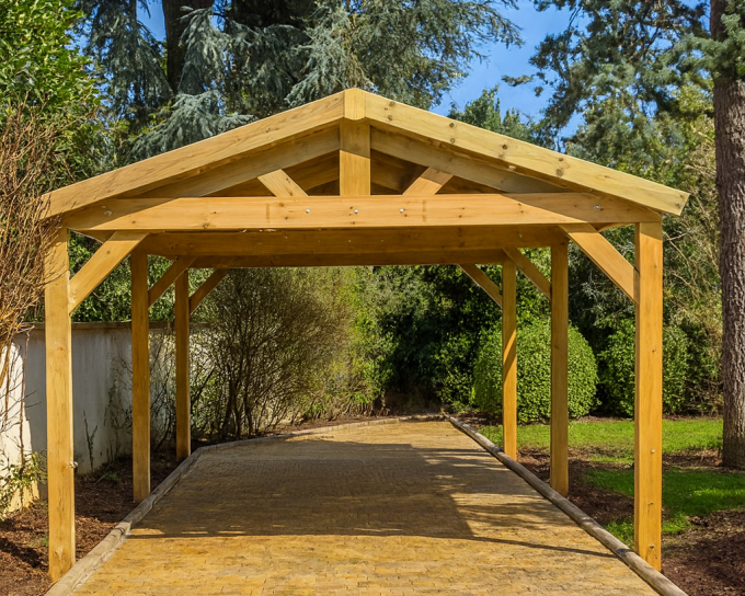 Carport en bois, allée pavée, verdure environnante.